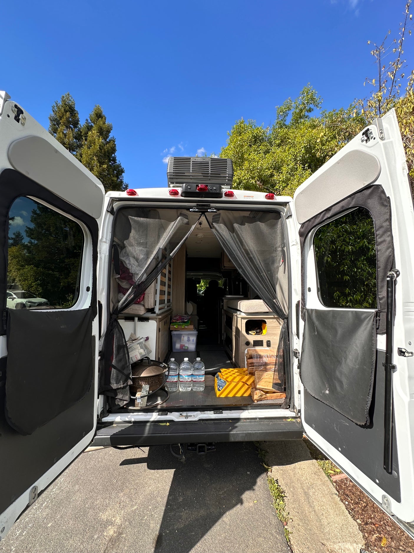 This rv rental shows its organized interior from the rear with open doors, ready for travel, including water and firewood.