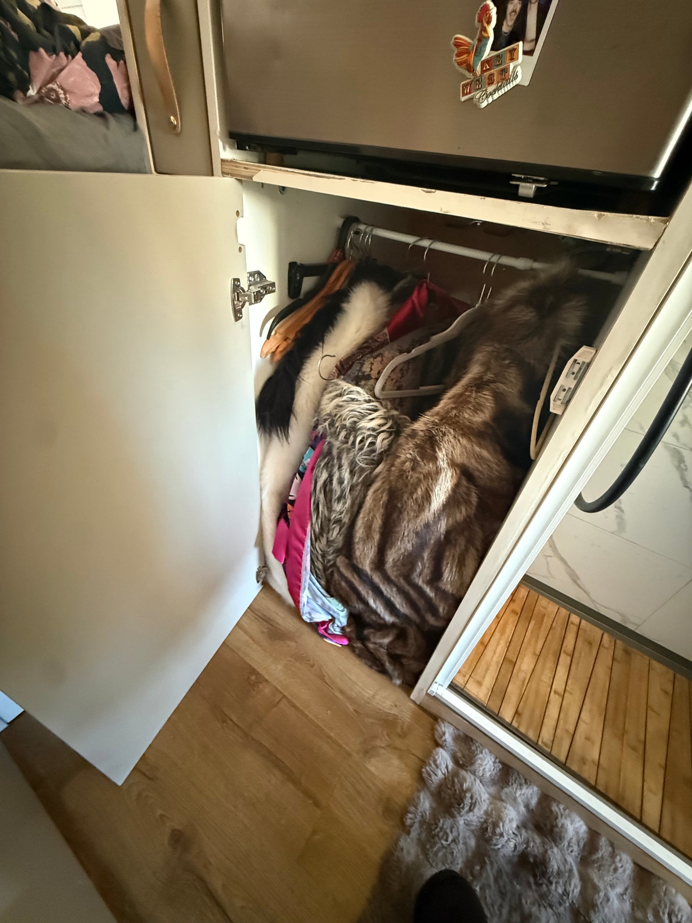 RV rental interior: A small open closet holds faux fur coats. Next to it, a compact shower and a fridge. Efficient storage.