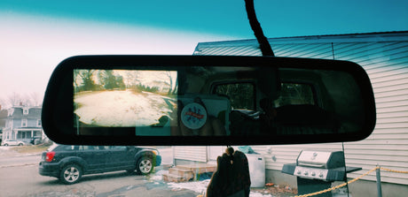 A cozy RV rental view: snowy road in the mirror, "Be Kind" message. Outside, an SUV, house, and grill complete the scene.