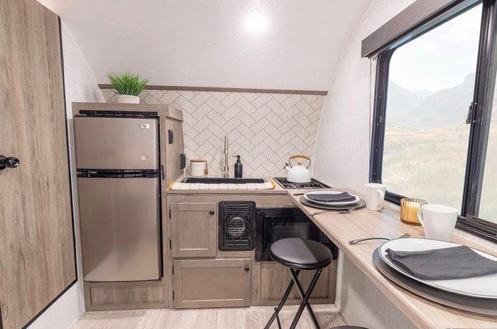 Experience this modern RV rental's kitchen. It features a fridge, sink, cooktop, microwave, and bar dining with a mountain view.