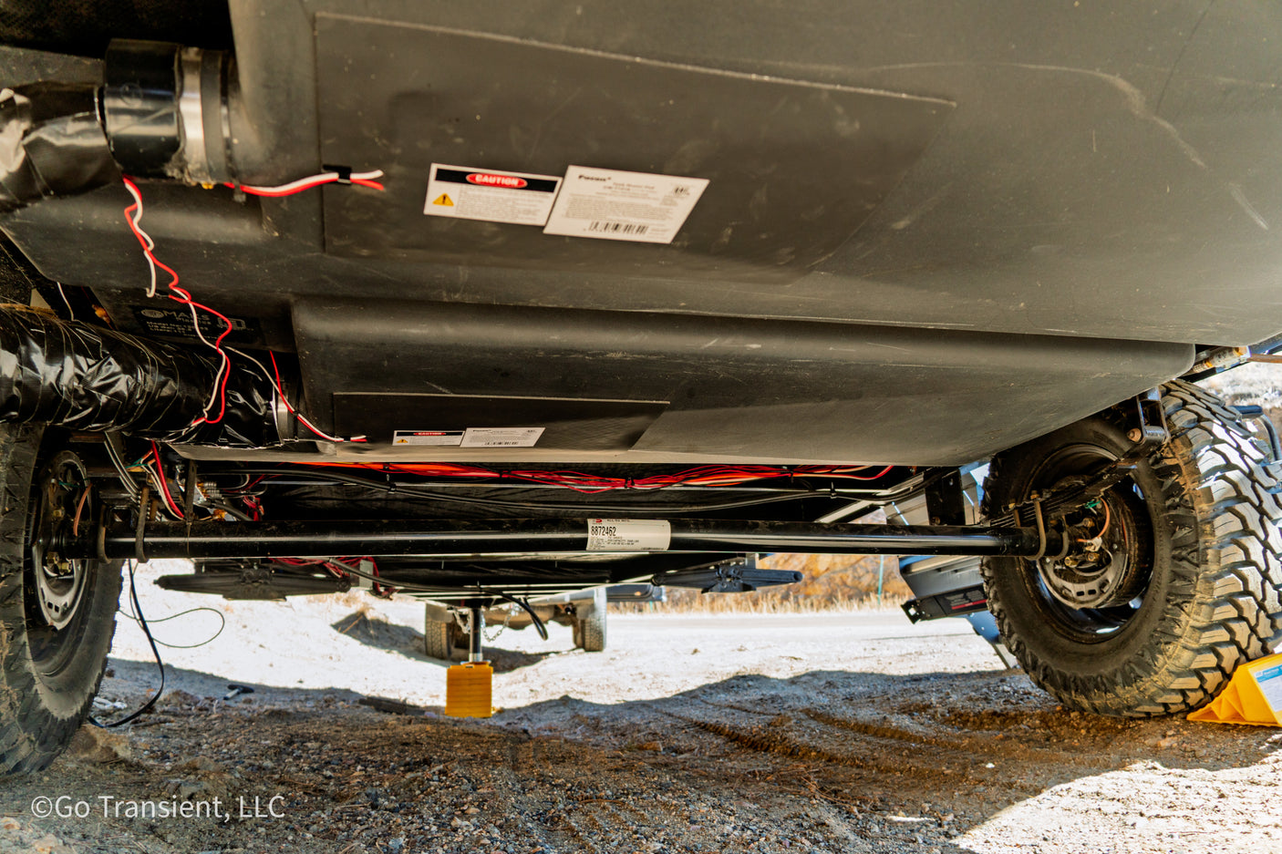 Underside view of an RV rental, revealing plumbing tanks, electrical wiring, and heavy-duty tires.