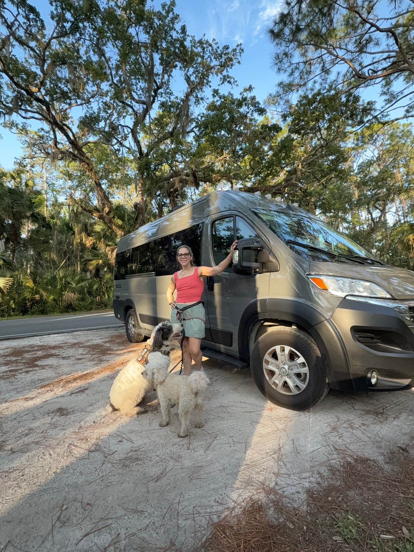 Exploring nature with pets! A woman and her two dogs pose by their RV rental under mossy trees.