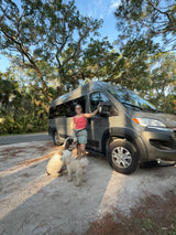 Exploring nature with pets! A woman and her two dogs pose by their RV rental under mossy trees.