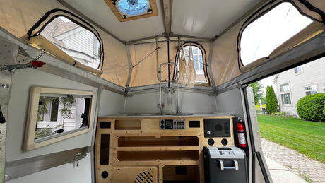 Compact pop-up camper interior: kitchen, controls, storage, and a fan, ready for your next rv rental adventure.