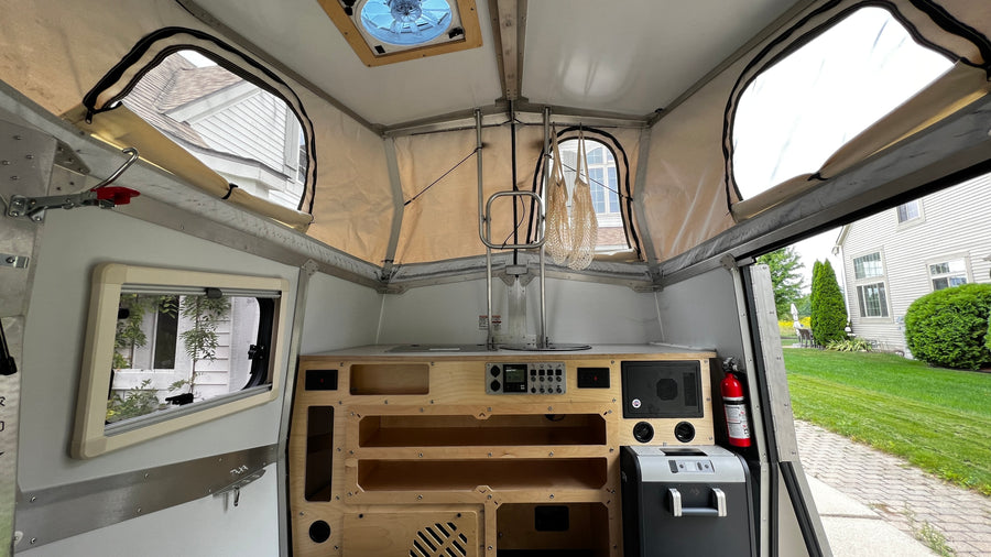 Compact pop-up camper interior: kitchen, controls, storage, and a fan, ready for your next rv rental adventure.
