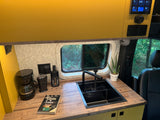 Cozy RV rental kitchen featuring a sink, coffee station, and nature view, perfect for adventure travel.