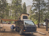 Pop-top VW camper van with awning at a scenic national park campsite. Your perfect RV rental for an outdoor adventure.