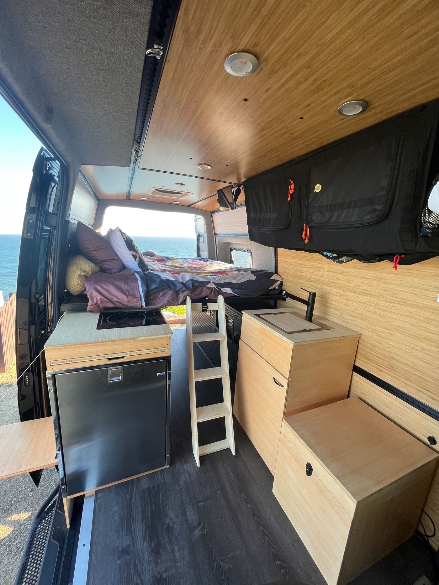 RV rental interior with a bed, kitchen, fridge, and stunning ocean views. Your cozy home on wheels. — photo 13