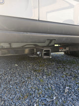 Close-up of a black Curt trailer hitch receiver mounted on an RV rental's rear, ideal for towing. Vehicle parked on gravel.