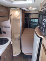 Compact RV rental interior: kitchen sink, wet bath with toilet, bed, microwave. Ideal for travel comfort.