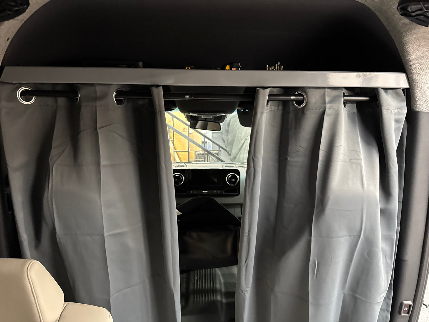 RV rental interior view: gray privacy curtains on a rod, separating the front cabin from the living area, with overhead storage.
