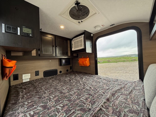 RV rental camper interior: a compact bedroom with controls, AC, and an open door offering an outdoor view.