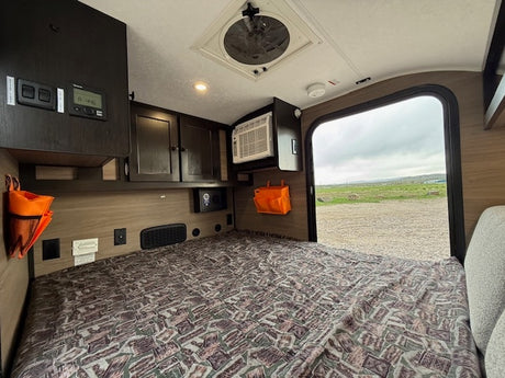 RV rental camper interior: a compact bedroom with controls, AC, and an open door offering an outdoor view.