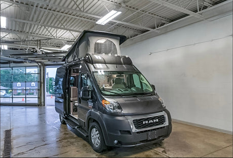 Gray Ram ProMaster camper van RV rental with pop-top roof, showcasing its interior from a service bay.