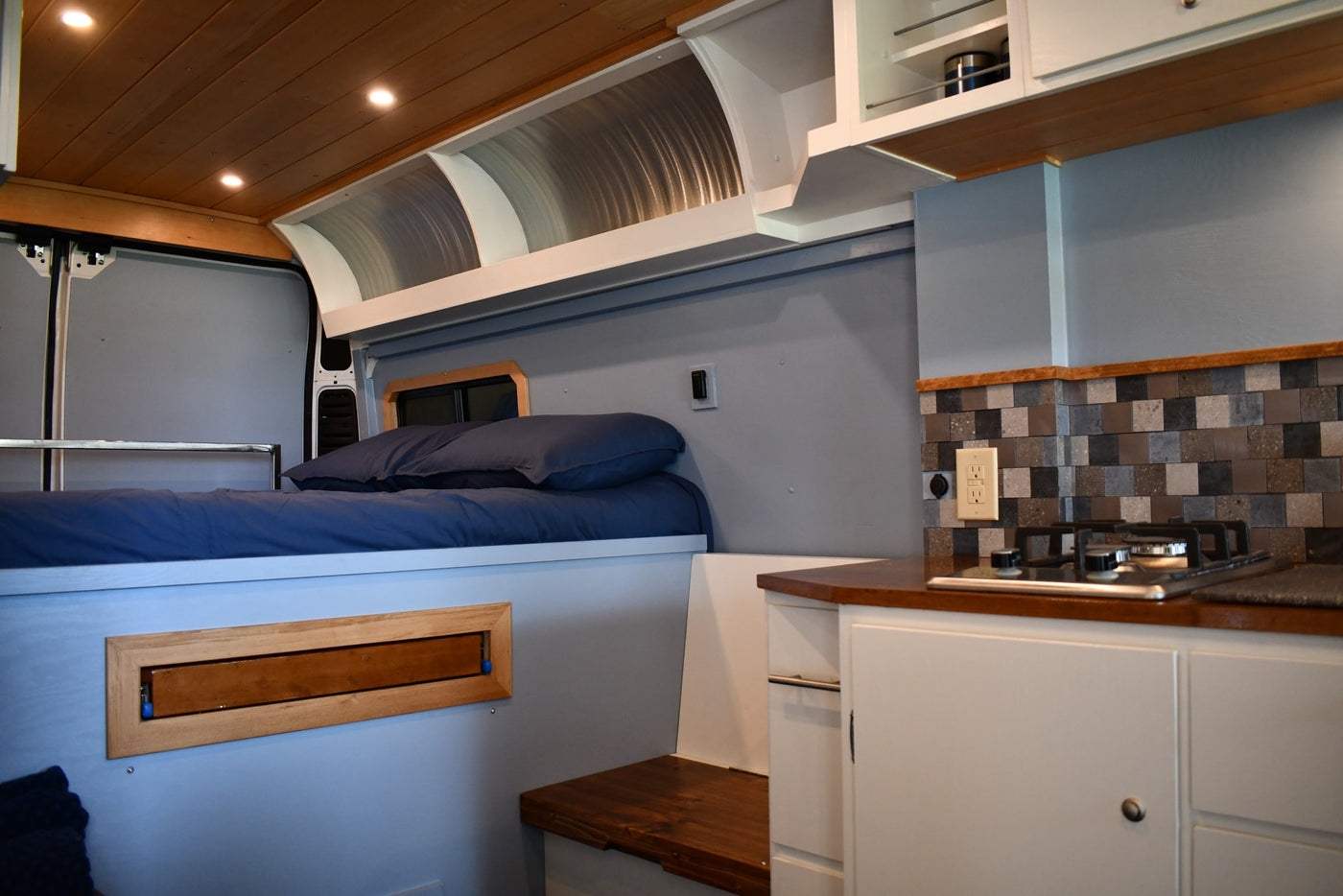 Experience comfort in this RV rental! Features a cozy bed, compact kitchen with a tiled backsplash, and smart overhead storage. — photo 6