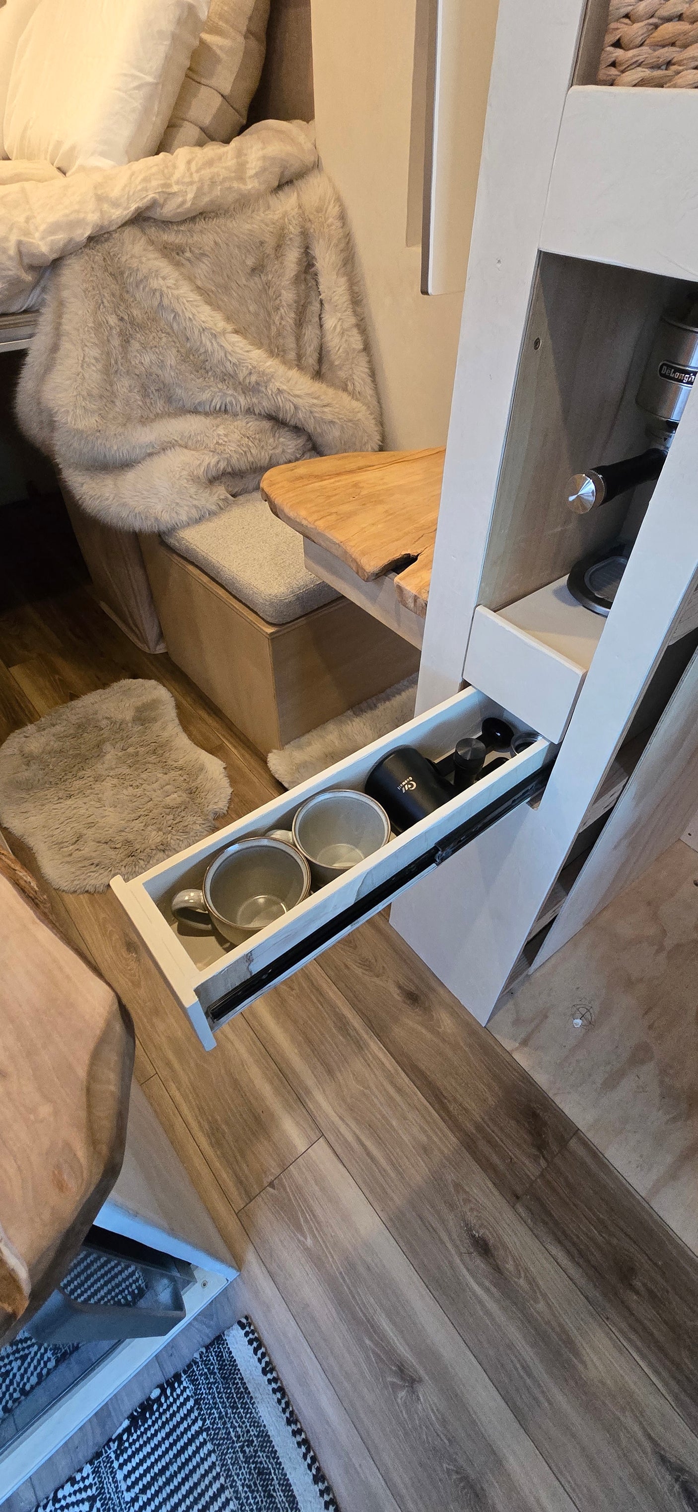 RV rental interior: A cozy coffee station with an espresso machine, mugs, wooden bench, and faux fur throw.