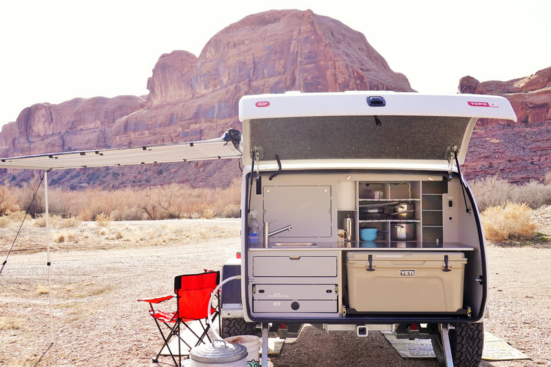 This RV rental camping trailer boasts an open outdoor kitchen with sink, Yeti cooler, and gear, set against desert mountains. — photo 8