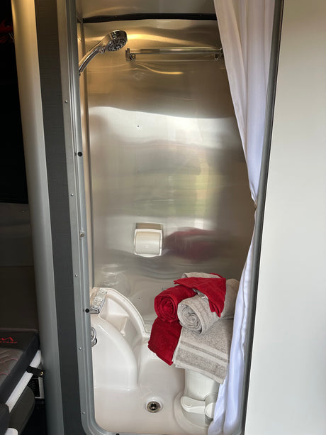 This RV rental showcases a compact, reflective metal shower/wet bath with a small sink, toilet, and fresh towels.