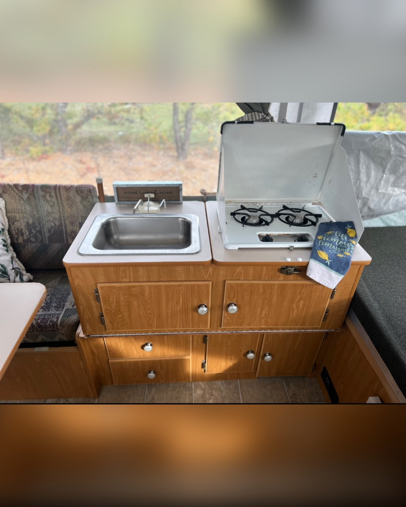 This RV rental features a cozy kitchen with a stainless steel sink, two-burner stove, and wooden cabinetry. Ideal for camping trips.