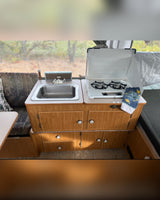 This RV rental features a cozy kitchen with a stainless steel sink, two-burner stove, and wooden cabinetry. Ideal for camping trips.