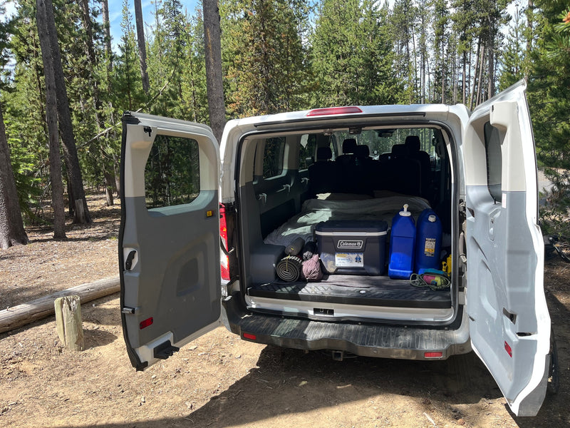 RV rental van packed for camping in the forest, featuring a bed, cooler, and water jugs. Ready for adventure! — photo 9