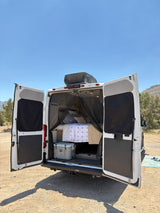 White RV rental's rear open, revealing a comfy bed, cooler, and mosquito net. Ideal for van life adventures.