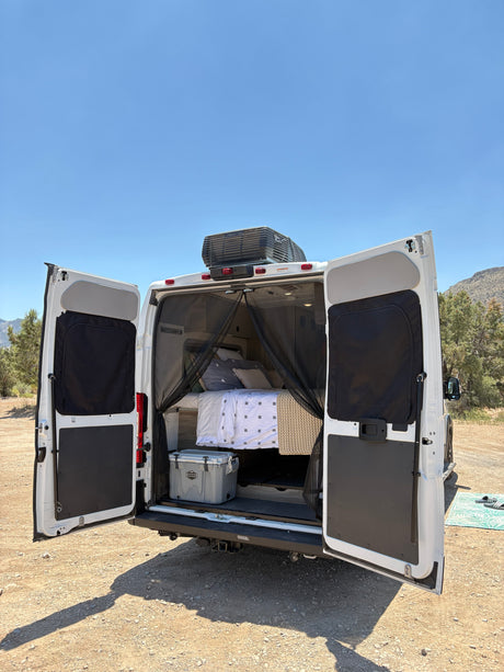 White RV rental's rear open, revealing a comfy bed, cooler, and mosquito net. Ideal for van life adventures.