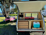 An rv rental teardrop camper's open galley with stove, cooler, and drawers, ready for outdoor cooking by a picnic table.