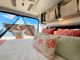 Enjoy stunning beach views from your comfortable RV rental. A happy girl smiles from inside, surrounded by cozy pillows.