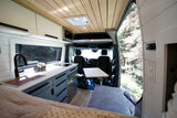 Spacious rv rental camper van interior with a modern kitchen, comfortable bed, and front table, all boasting forest views.