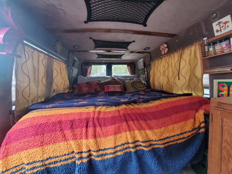 This inviting RV rental features a cozy bed with a cheerful striped blanket and eclectic decor.