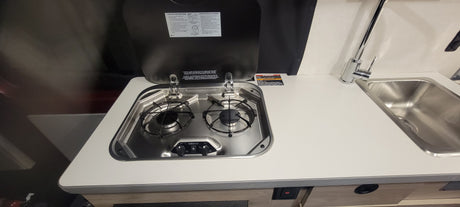 Inside an RV rental: a compact kitchen with a two-burner gas stove (Suburban) and stainless steel sink. Ideal for travel.