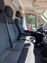 RV rental van's front cabin: gray and black seats, steering wheel, ceiling track for storage/curtains. A red truck is outside.
