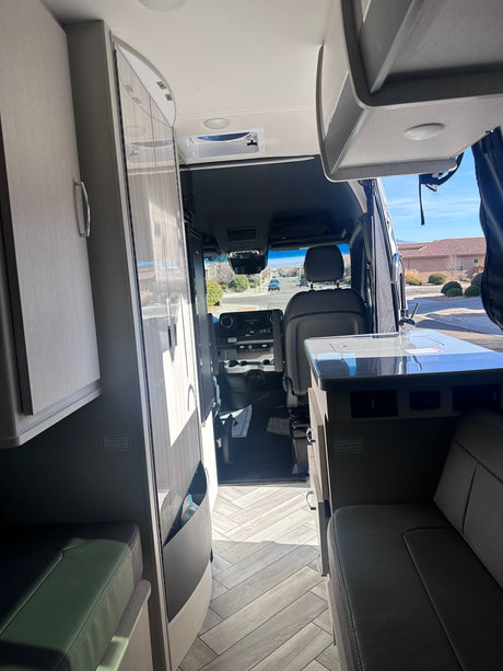 Modern RV rental interior, showing the cockpit, kitchenette, and seating from the rear of the vehicle.