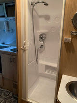 This RV rental interior features a compact shower stall and a small kitchen area with twin sinks.