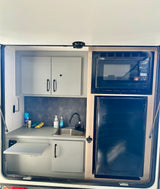 Compact RV rental outdoor kitchen with sink, microwave, fridge, pull-out shelf, and storage for convenient camping.