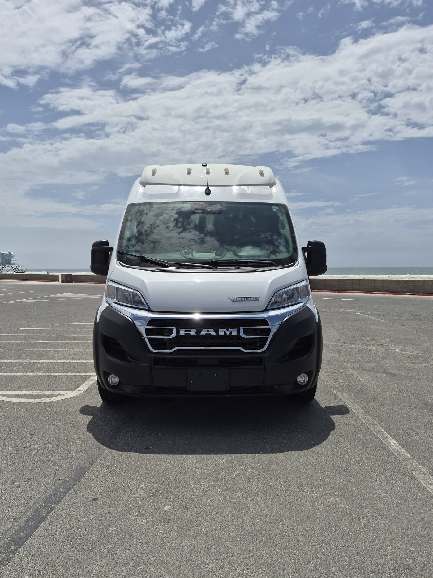 ready for adventure.|A white Winnebago Ram Promaster camper van (rv rental) parked by the ocean on a cloudy day.|This white RAM camper van — photo 2
