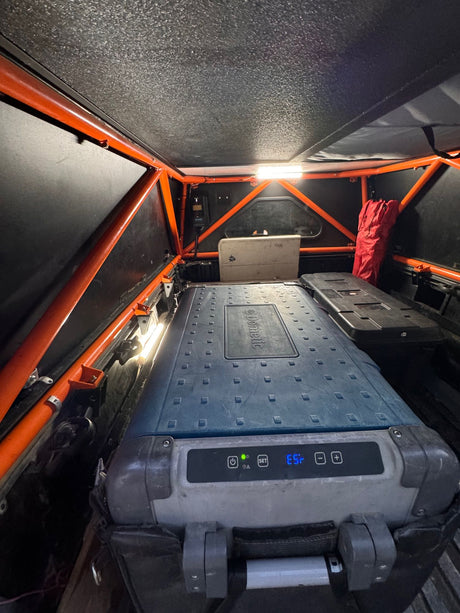 RV rental camping setup: truck bed with Dometic portable fridge, bright lights, & rugged orange roll cage for overlanding.
