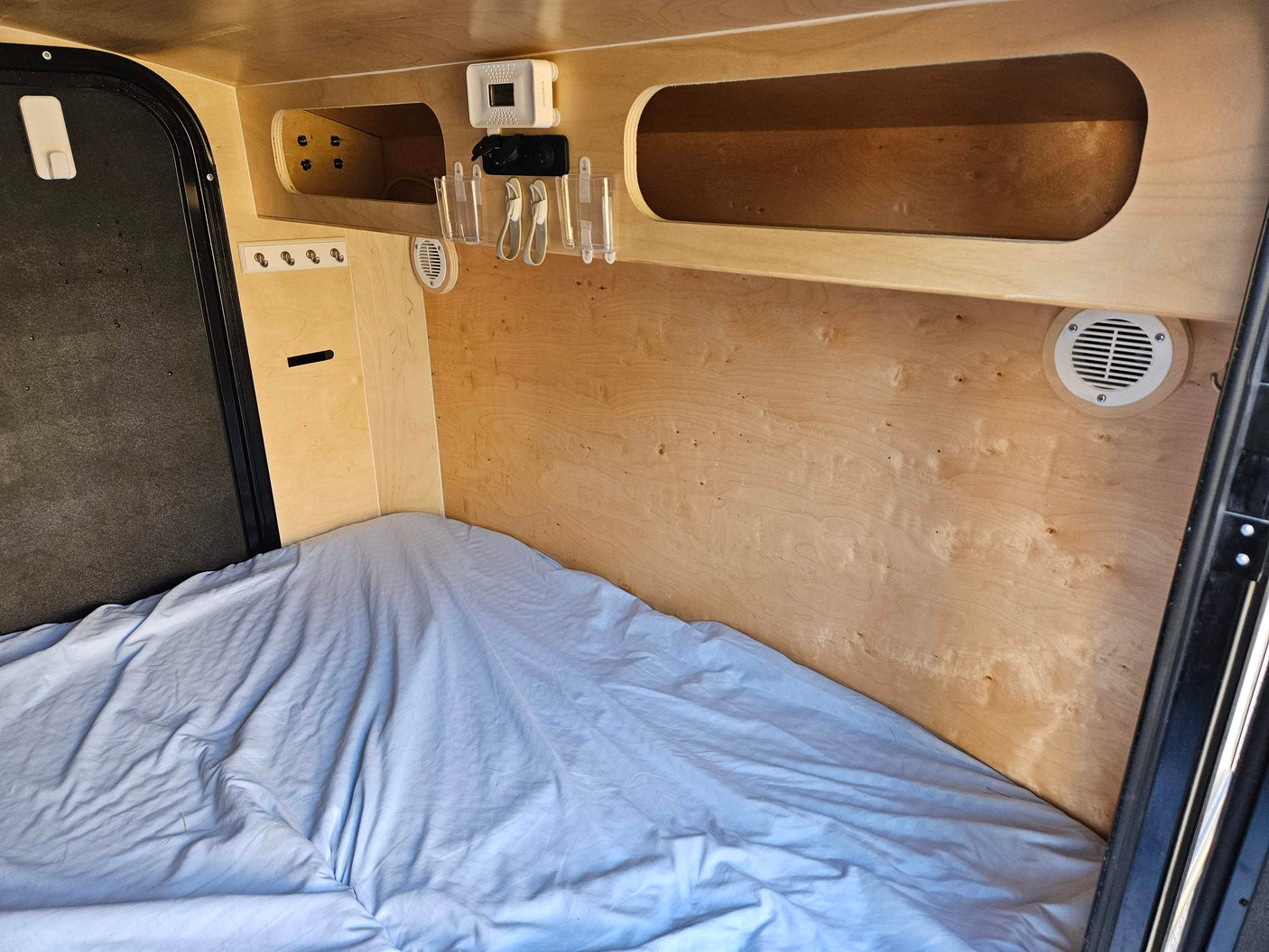 Inside a cozy RV rental: bed, wood walls, CO detector, charging port, and storage. Ideal for adventurers.