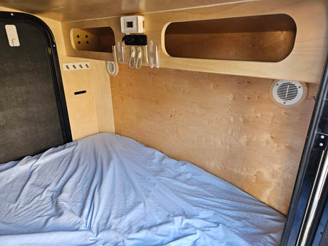 Inside a cozy RV rental: bed, wood walls, CO detector, charging port, and storage. Ideal for adventurers.