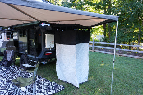 Spacious RV rental setup: an extended awning shades a camper trailer with a mounted water heater and portable outdoor shower. Camping ready!