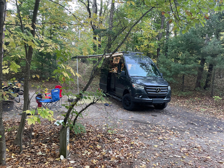 This rv rental is set up at a forest campsite (site 508) with chairs, fire pit, and autumn leaves.