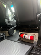 RV rental van interior showing front seats, grey textured flooring, and a red fire extinguisher securely mounted by the passenger seat base for safety.