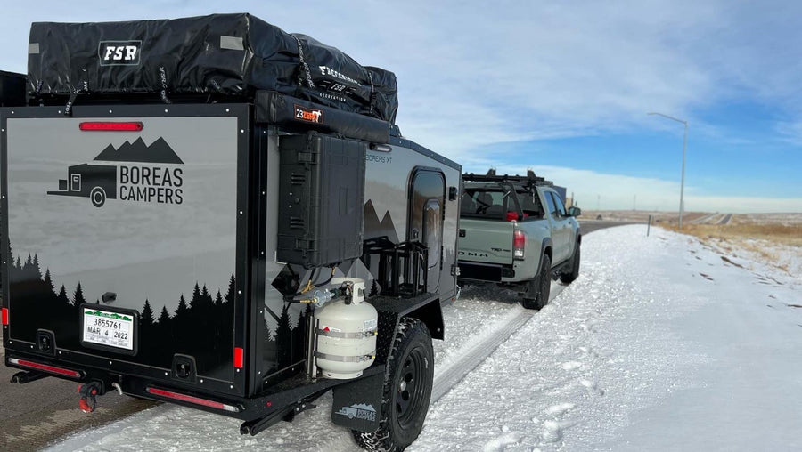 An off-road camper trailer and truck on a snowy road, ready for winter adventure. Consider this RV rental for your travels!