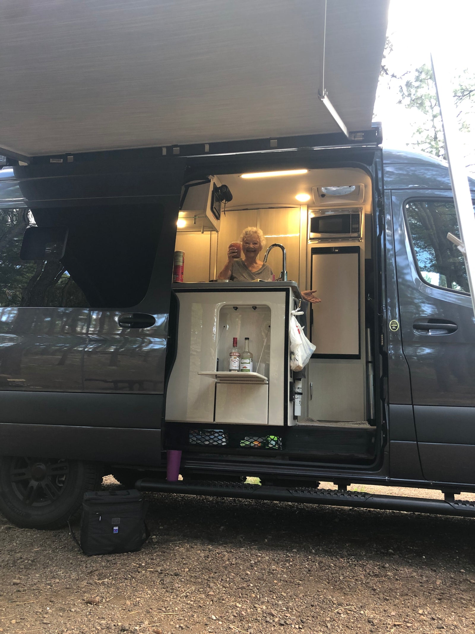 Happy woman in her spacious RV rental's mobile kitchen, complete with sink, microwave, fridge, and awning for camping enjoyment.