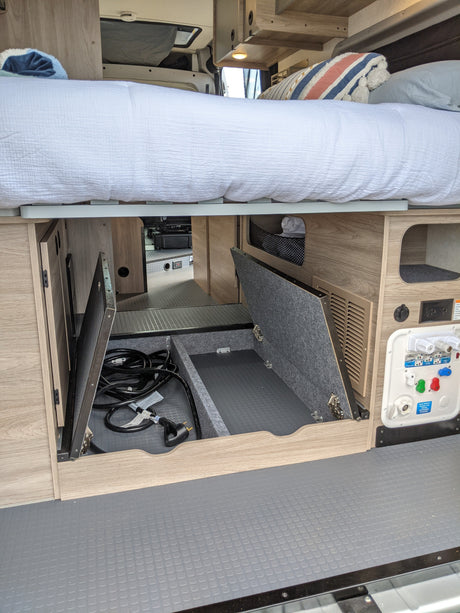 Under-bed storage and a utility panel with electrical/water hookups in a clean rv rental, ideal for organizing gear.