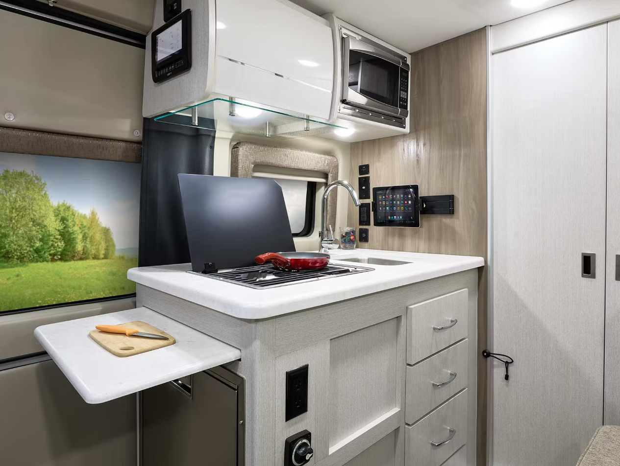 This modern RV rental kitchen features a sink, stovetop, microwave, and pull-out cutting board, perfect for mobile living. — photo 14