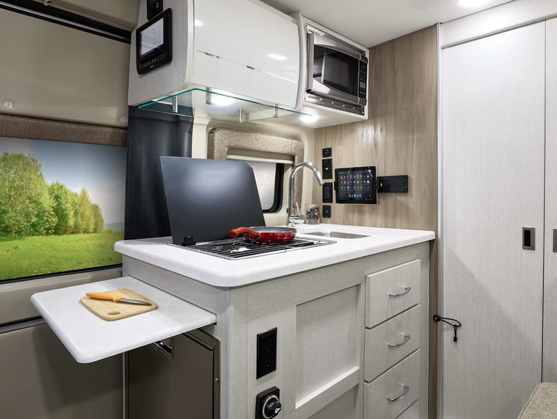 This modern RV rental kitchen features a sink, stovetop, microwave, and pull-out cutting board, perfect for mobile living. — photo 14