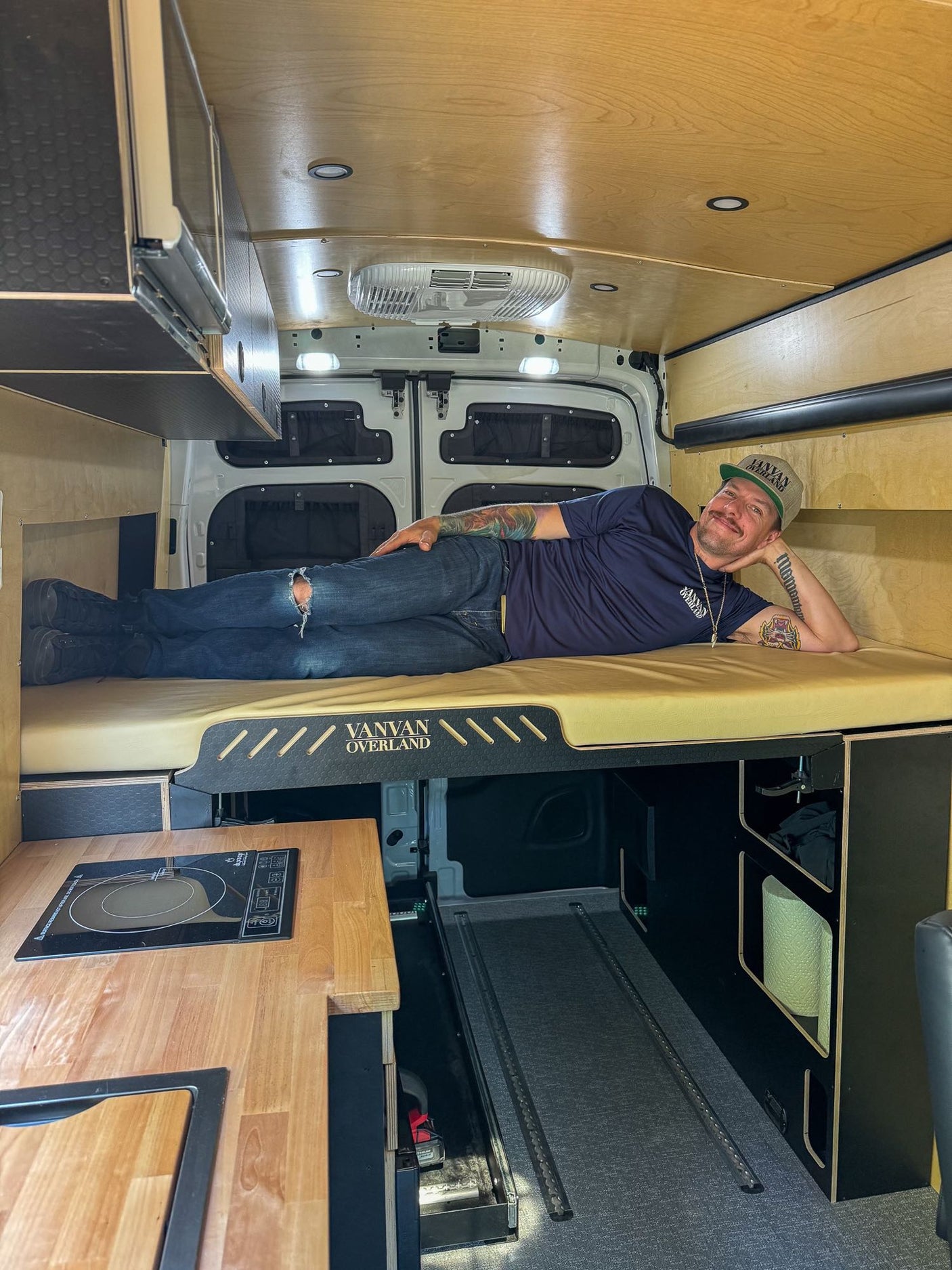 Inside an RV rental, a man relaxes in a custom camper van with a cozy bed & kitchen.