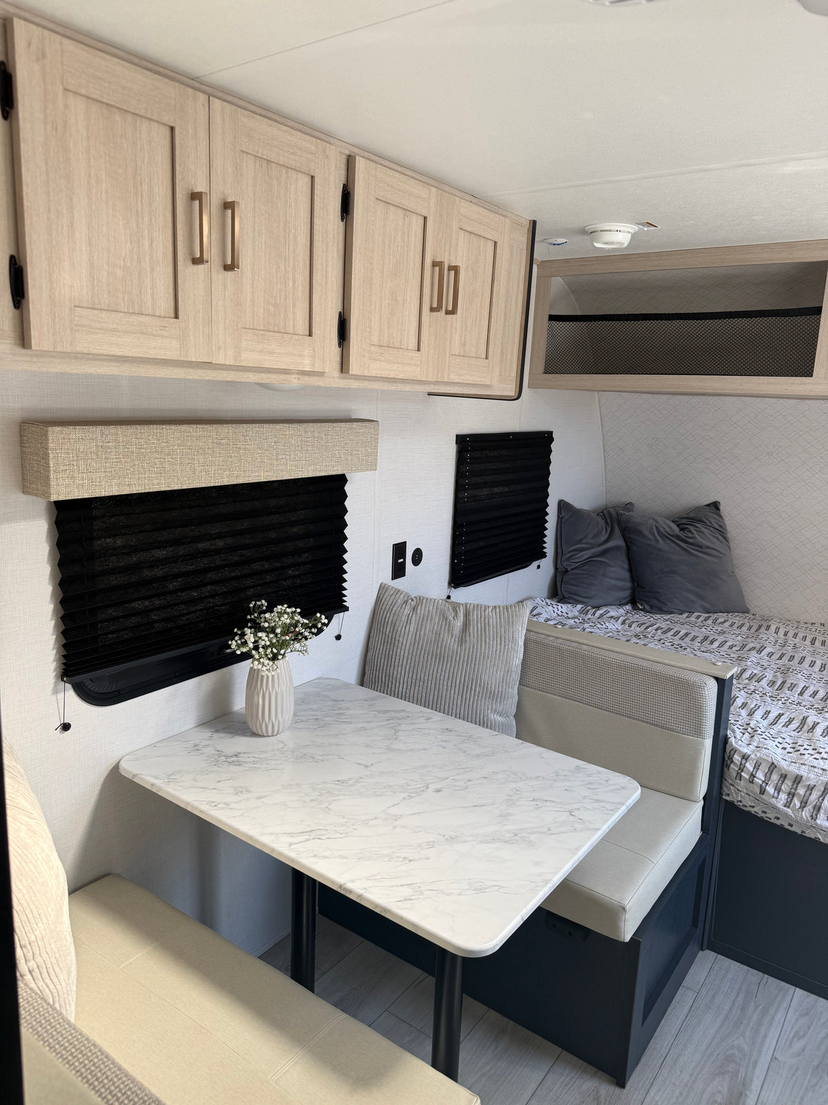 Light and airy rv rental interior featuring a dinette with a marble-look table, overhead cabinets, and a cozy bed with pillows. — photo 3